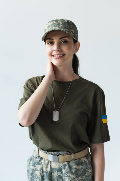 Positive soldier with ukrainian flag on uniform smiling at camera isolated on grey 