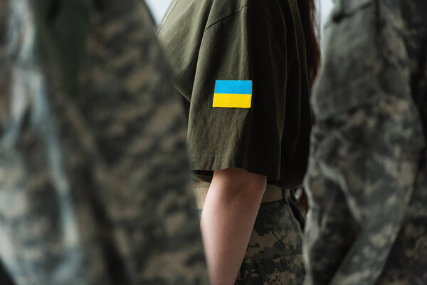 Cropped view of servicewoman with ukraining flag on chevron standing near soldiers isolated on grey 