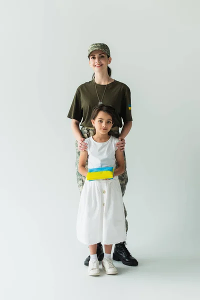Smiling Woman Camouflage Uniform Hugging Daughter Ukrainian Flag Grey Background — Photo