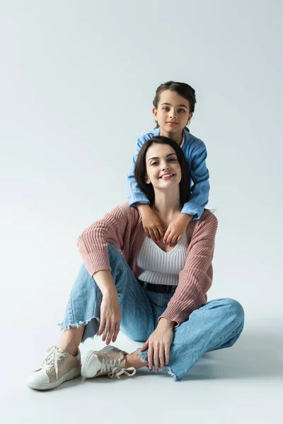 Child Looking Camera Embracing Mother Sitting Jeans Grey Background — Fotografia de Stock