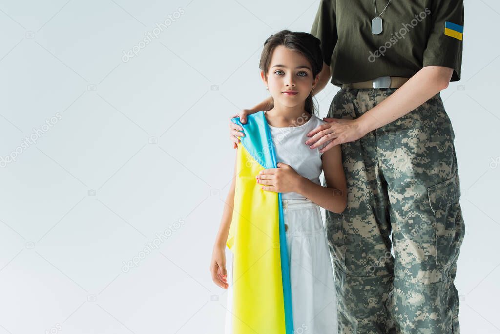 Soldier hugging child with ukrainian flag isolated on grey 