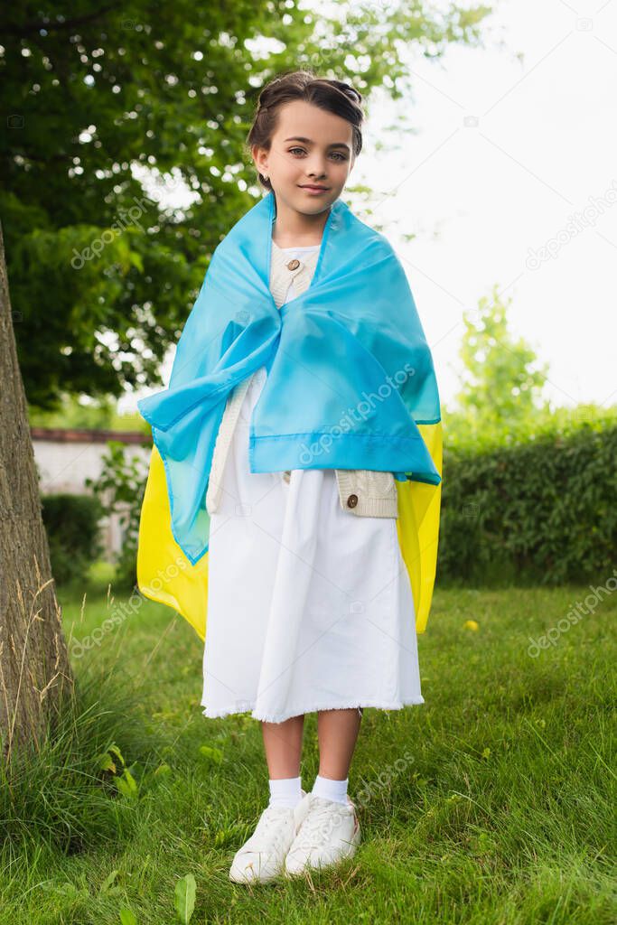 full length of patriotic child covered with ukrainian flag in park