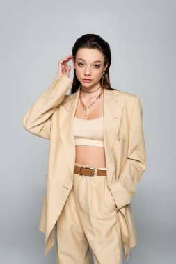 pretty young woman in beige blazer posing with hand in pocket isolated on grey