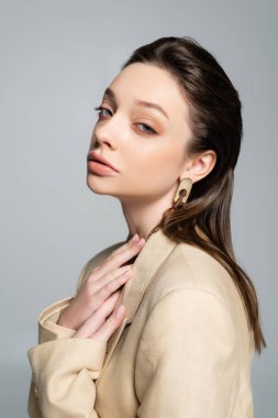 sensual young woman in beige blazer looking at camera isolated on grey