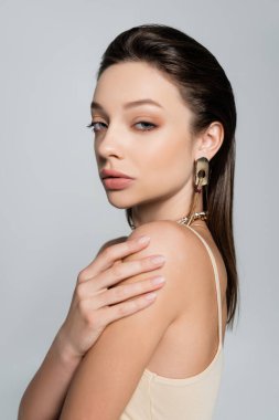 brunette woman in trendy accessories posing isolated on grey