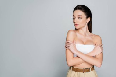 pretty young woman with bare shoulders and makeup looking away isolated on grey