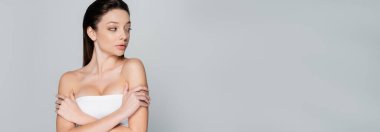 pretty young woman with bare shoulders and makeup looking away isolated on grey, banner