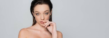 portrait of young woman with bare shoulders and makeup looking at camera isolated on grey, banner