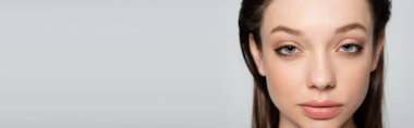 close up view of young woman with blue eyes and makeup isolated on grey, banner