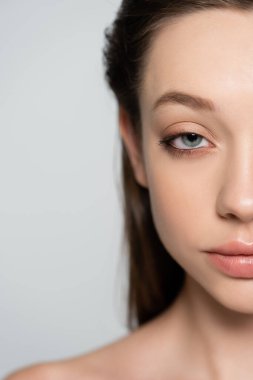 cropped view of young woman with blue eye and bare shoulder isolated on grey