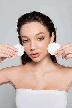 pretty young woman removing makeup with cotton pads isolated on grey clipart
