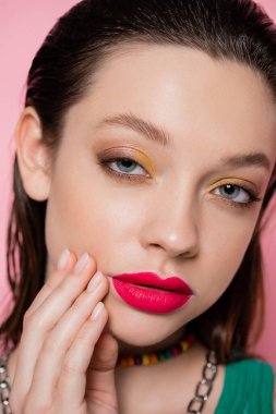 close up view of young brunette woman with bright makeup looking at camera isolated on pink 