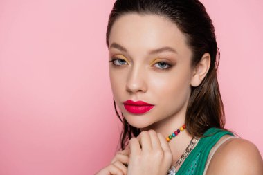 young brunette model with bright makeup looking at camera isolated on pink 