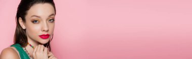 young brunette model with bright makeup looking at camera isolated on pink, banner