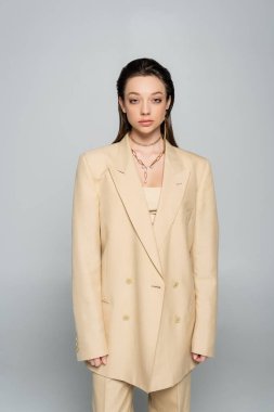 brunette woman in stylish outfit with beige blazer posing isolated on grey