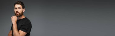 portrait of pensive man in black t-shirt looking away isolated on grey, banner