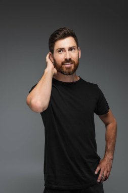 portrait of smiling bearded man in black t-shirt looking away isolated on grey
