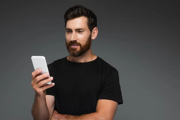 Smiling Bearded Man Black Shirt Looking Smartphone Isolated Grey — Stock Photo, Image