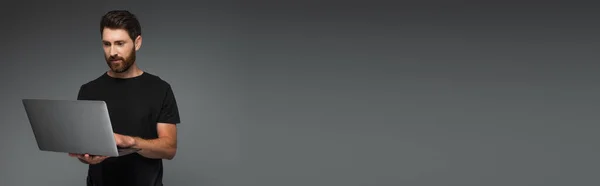 Бородатый Мужчина Черной Футболке Помощью Ноутбука Изолированного Сером Баннер — стоковое фото