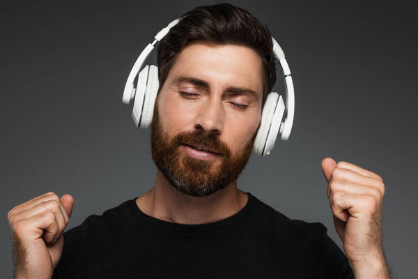 bearded man with closed eyed listening music in wireless headphones isolated on grey