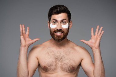 excited bearded man with moisturizing eye patches gesturing isolated on grey 