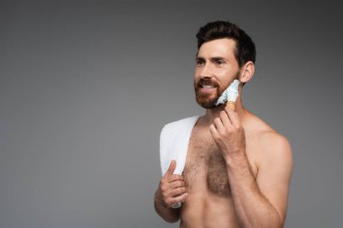 happy bearded man with towel applying shaving foam with shaving brush isolated on grey