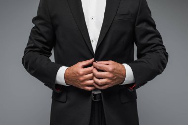 cropped view of elegant man in black tuxedo adjusting blazer isolated on grey