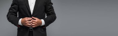 cropped view of elegant man in black tuxedo adjusting blazer isolated on grey, banner