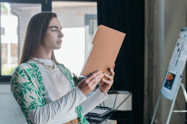 Queer designer holding paper folder in creative agency 