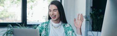 Positive nonbinary designer having video call on laptop in office, banner 