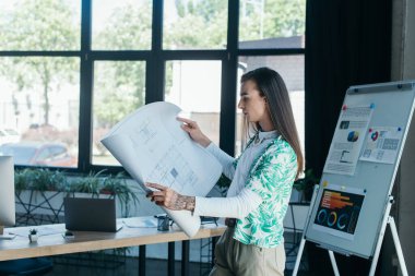 Side view of nonbinary designer holding blueprint in creative agency 