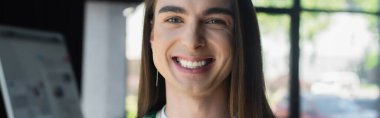 Cheerful nonbinary designer looking at camera in creative agency, banner 