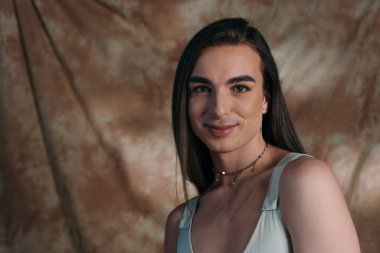 Portrait of brunette queer person looking at camera on abstract background 