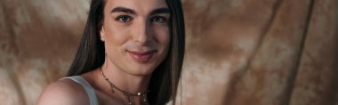 Positive queer person looking at camera on abstract background, banner 