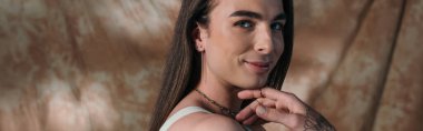 Portrait of smiling brunette queer person on abstract background, banner 