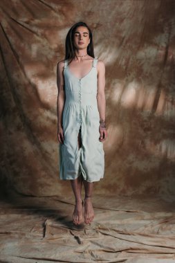 Brunette nonbinary person in dress jumping on abstract brown background 