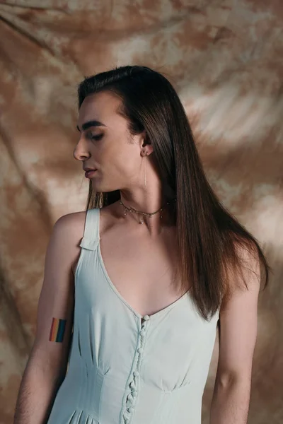 Side view of brunette queer person in dress standing on abstract background