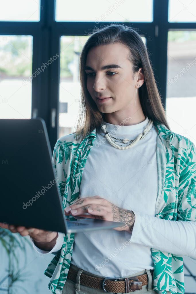 Brunette queer designer using blurred laptop in creative agency 