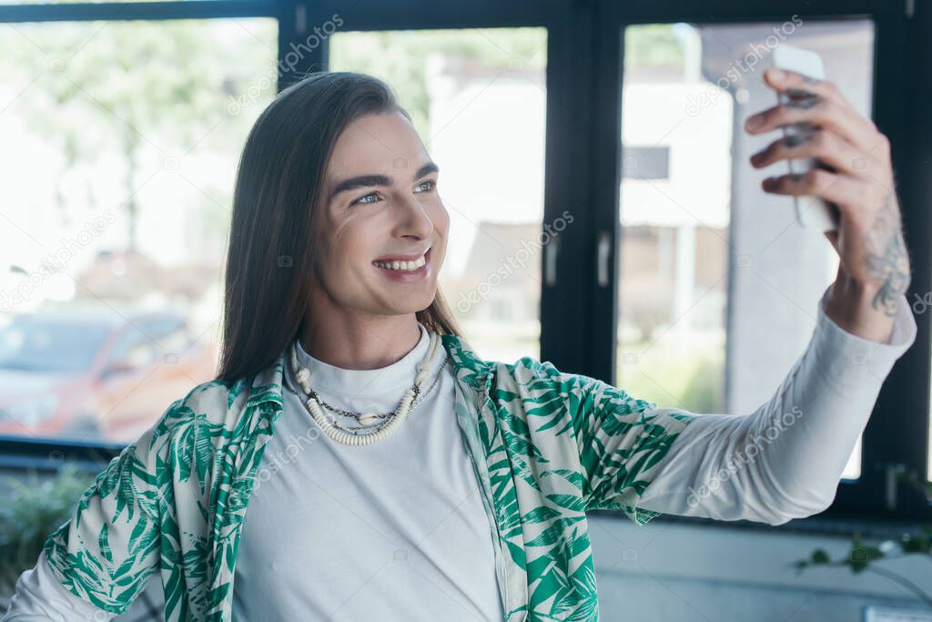 Cheerful queer designer using blurred smartphone in creative agency 
