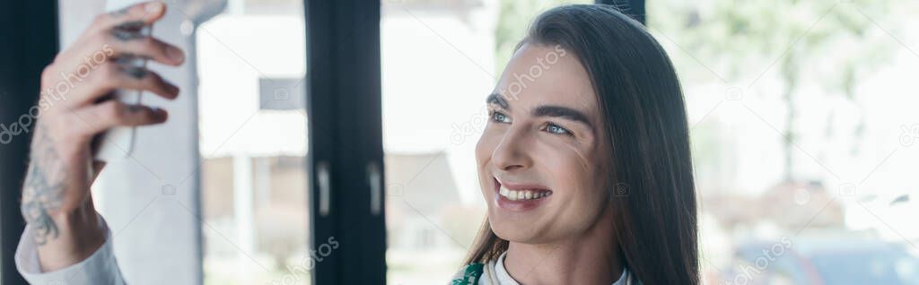 Positive nonbinary designer holding smartphone in office, banner 