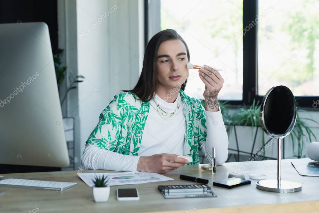Queer designer applying makeup near devices in office 