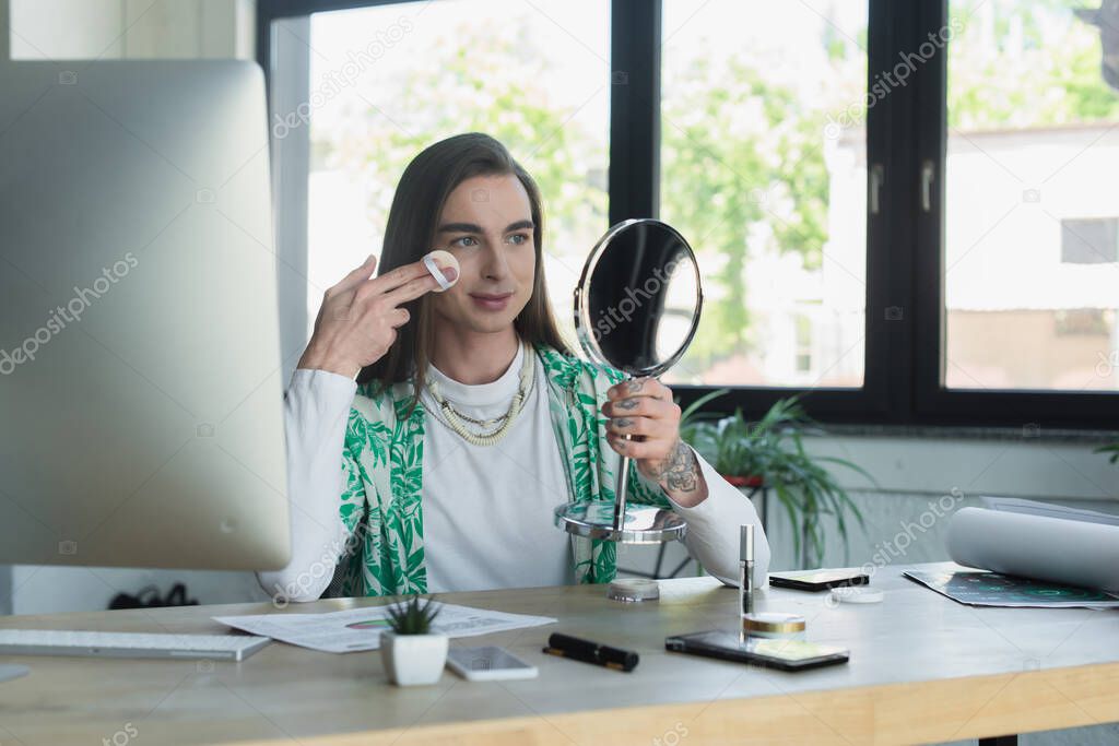 Queer person applying makeup near devices in creative agency in office 