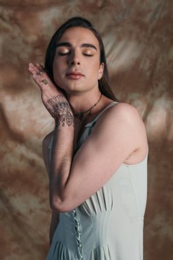 Portrait of stylish queer person in dress posing on abstract brown background 