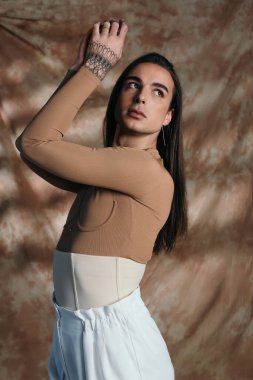 Brunette nonbinary person in corset posing on abstract brown background 