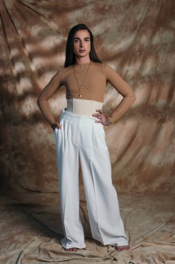 Trendy nonbinary person in corset posing and looking at camera on abstract brown background 