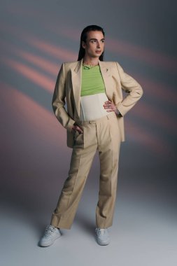 Full length of trendy queer person in suit standing on abstract background 