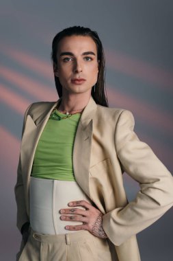 Stylish queer person in suit looking at camera on abstract background 