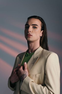 Portrait of brunette queer person in jacket standing on abstract background 