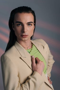 Young nonbinary person in jacket looking at camera on abstract background 