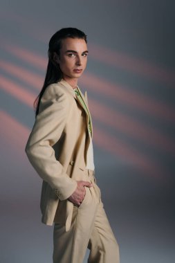 Stylish queer model in suit looking at camera on abstract background 
